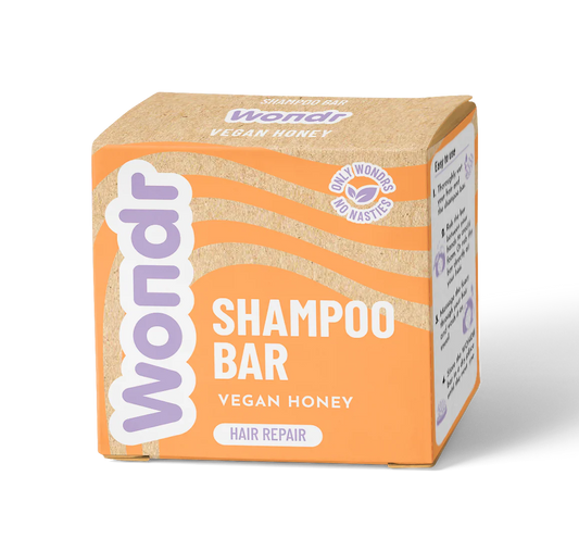 A packaged shampoo bar labeled 'WONDR SHAMPOO BAR VEGAN HONEY' with additional text 'HAIR REPAIR'. The packaging is predominantly orange with a transparent window revealing the light brown bar inside.