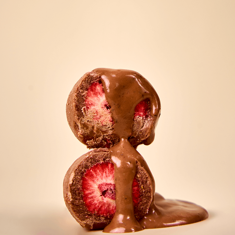 Bitten strawberries covered in Karü milk chocolate, shown frontally with visible interiors and melted chocolate dripping over them.