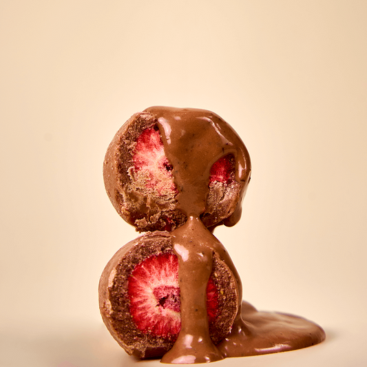 Bitten strawberries covered in Karü milk chocolate, shown frontally with visible interiors and melted chocolate dripping over them.